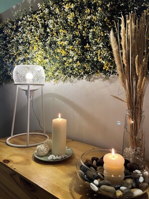 Une table éclairée à la bougie, avec un mur décoratif et un vase contenant des plantes séchées.