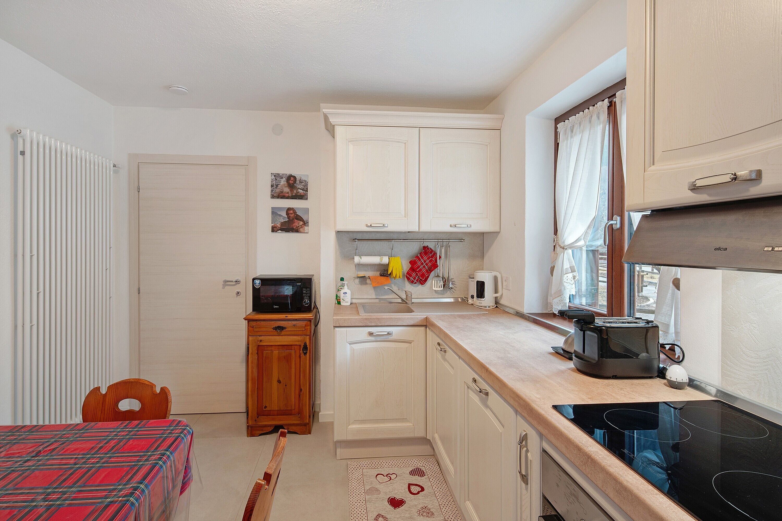 Cocina compacta con microondas, tostadora y estufa, armarios de madera y una zona de comedor con mantel escocés.