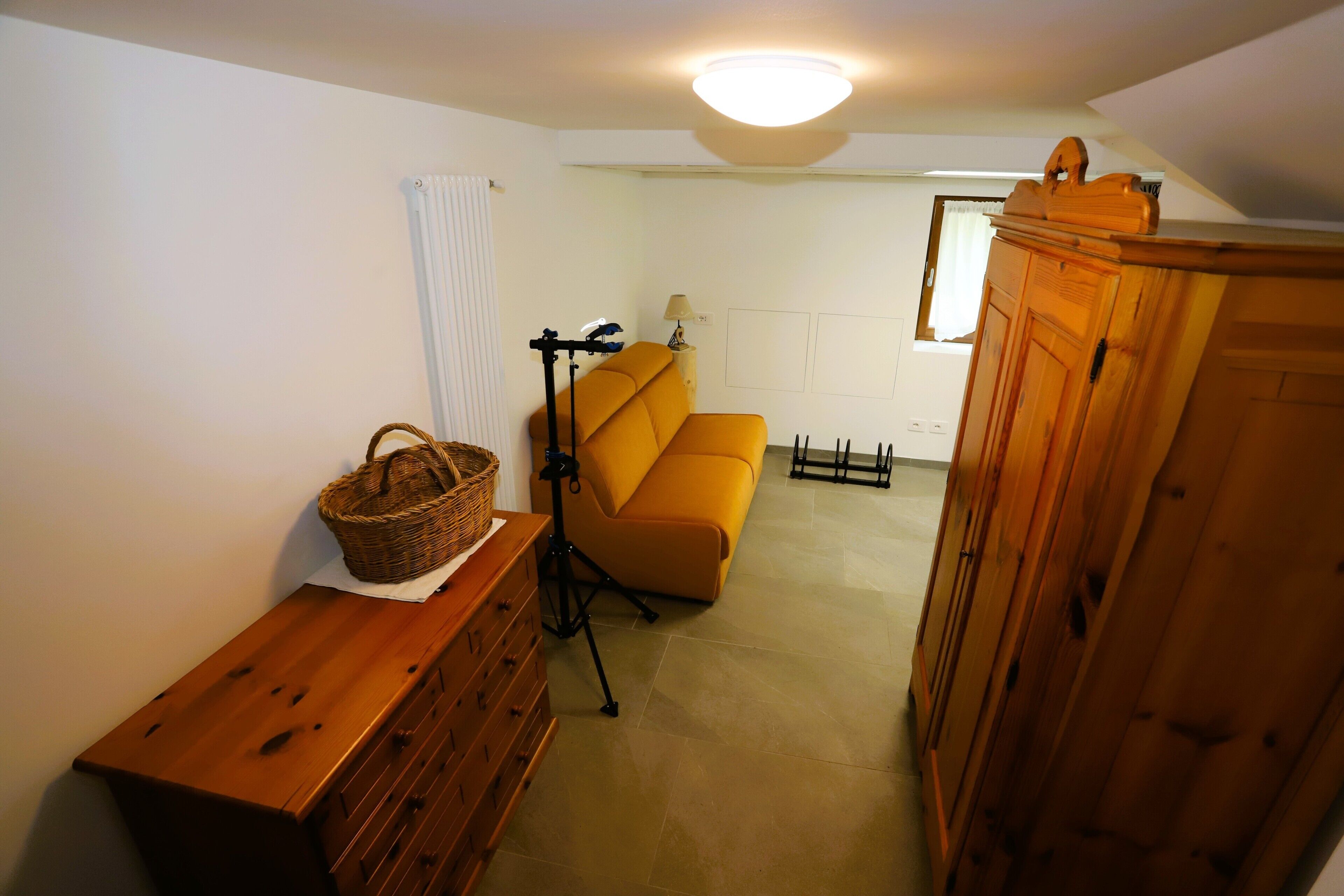Ein Zimmer mit einem Holzkoffer, einem Korbwäschesammler, einem Stativ und einem gelben Sofa.