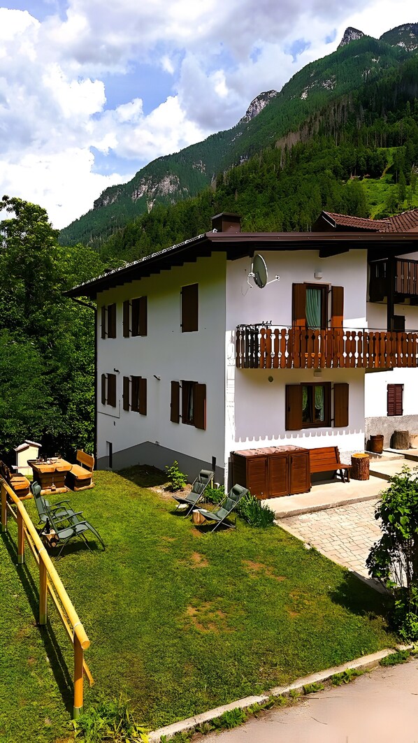 Ein zweistöckiges Gebäude mit Balkon, einem Garten mit Stühlen und einem Blick auf die Berge.