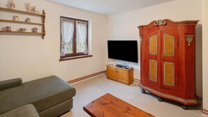 Ein Wohnzimmer mit einer Couch, einem Holzschrank, einem Fernseher und einem Fenster mit Vorhängen.