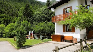 Ein zweistöckiges Gebäude mit Balkon, umgeben von Grünpflanzen und Bergen.