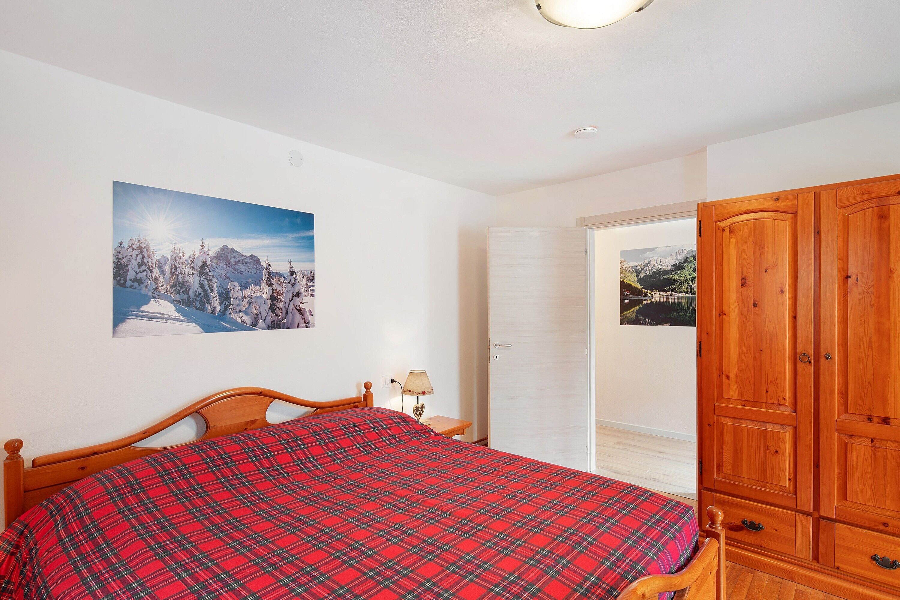 Un dormitorio con una cama, un armario de madera, una mesita de noche con lámpara y un cuadro en la pared.
