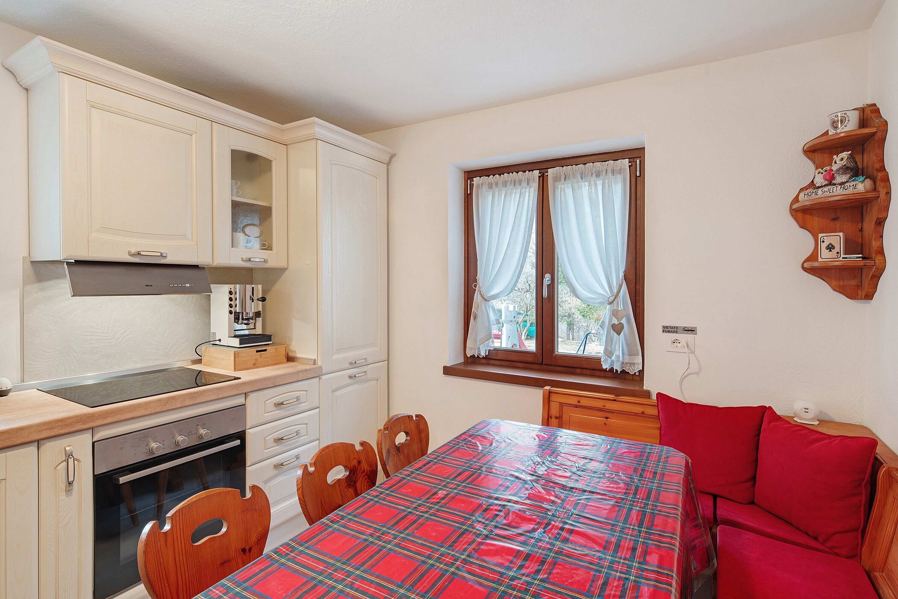 A kitchen with wooden cabinets, a stove, and a dining area with a plaid tablecloth and wooden chairs.