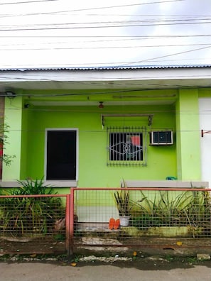 A house with a green facade, a small window with a metal grill, and a visible door.