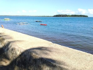 A concrete waterfront with boats on the water and a distant island.