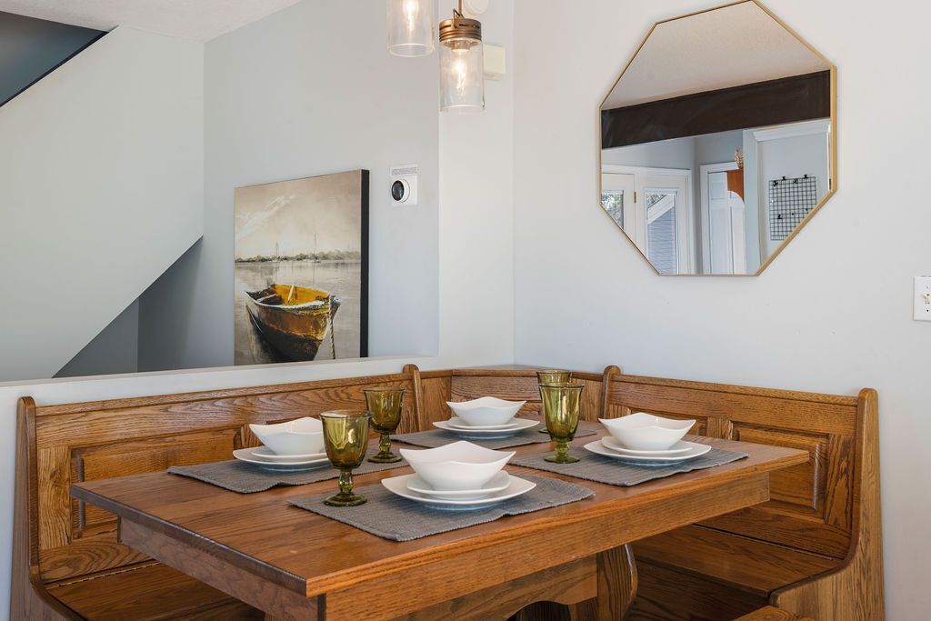 A dining area with a wooden table set for four, a painting on the wall, and a mirror reflecting the room.