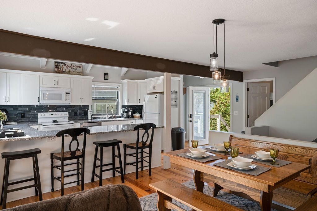 A modern kitchen with white cabinets, a central island, bar stools, and a dining table set for four.