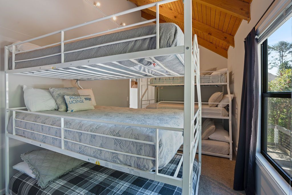 A bunk bed room with a window, a wooden ceiling, and a small table with a chair.