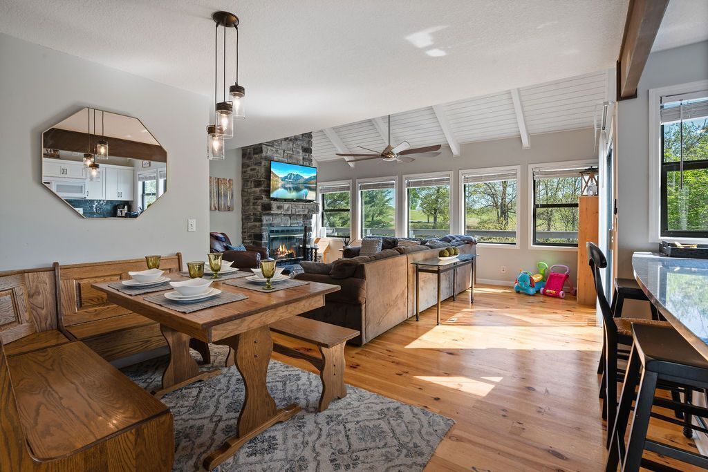 A spacious living area with a wooden dining table, a sofa, and a TV mounted on a stone wall.