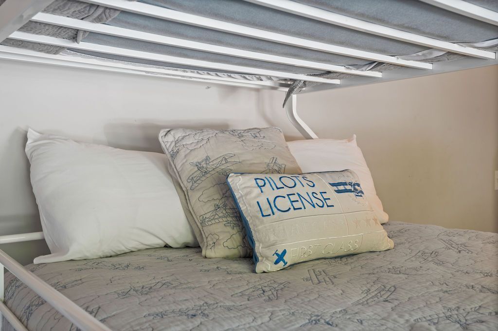 Una cama con una colcha y almohadas estampadas, incluyendo una con el texto 'Pilots License'.