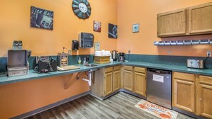A compact kitchen with wooden cabinets, a coffee machine, a toaster, and a clock on the wall. - The Roosevelt Hotel & RV Park Gateway to Theodore Roosevelt National Park-Medora-on i-94 (Wibaux)