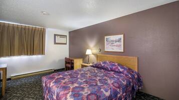 A hotel room with a bed, a nightstand, a lamp, a window with curtains, and a painting on the wall.