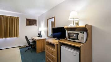 A hotel room with a desk, chair, television, microwave, refrigerator, and a bed.