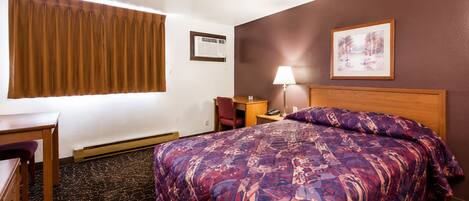 Habitación de hotel con cama, escritorio, silla, lámpara, equipo de aire acondicionado y un cuadro en la pared.