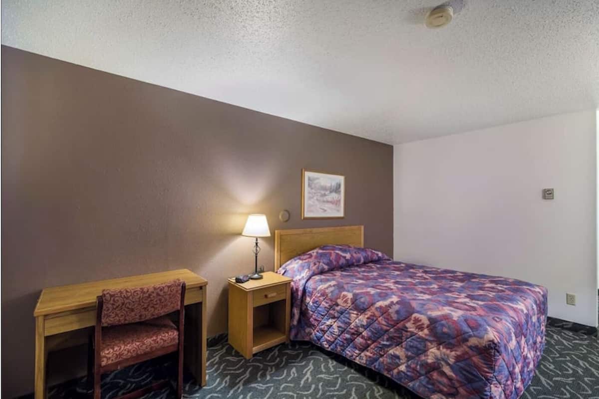 Ein Hotelzimmer mit einem Bett, einem Schreibtisch, einem Stuhl, einem Nachttisch mit Lampe sowie einem Wandbild.