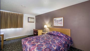 Ein Hotelzimmer mit einem Bett, einem Schreibtisch, einem Stuhl, einer Lampe und zwei gerahmten Bildern an der Wand.
