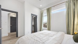 Ein Schlafzimmer mit Bett, einer Tür zu einem anderen Raum und einem Fenster mit Vorhängen.