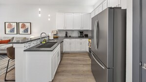 Eine moderne Küche mit weißen Schränken, einem Edelstahlkühlschrank und einer zentralen Kochinsel mit Spüle.