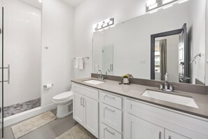 Ein modernes Badezimmer mit begehbarer Dusche, Toilette und einem Waschtisch mit zwei Becken und einem großen Spiegel.