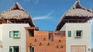Un edificio con due strutture a tetto di paglia su entrambi i lati, un muro centrale in mattoni con aperture triangolari e un'unica porta garage.