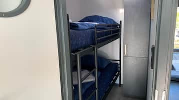 Ein Stockbett mit Metallgestell und blauer Bettwäsche, ein kleiner Schrank und eine Tür zu einem Außenbereich.