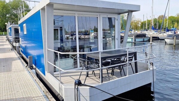 Eine moderne, schwimmende Konstruktion mit Glasfassade, einem Tisch und Stühlen auf einem Steg.