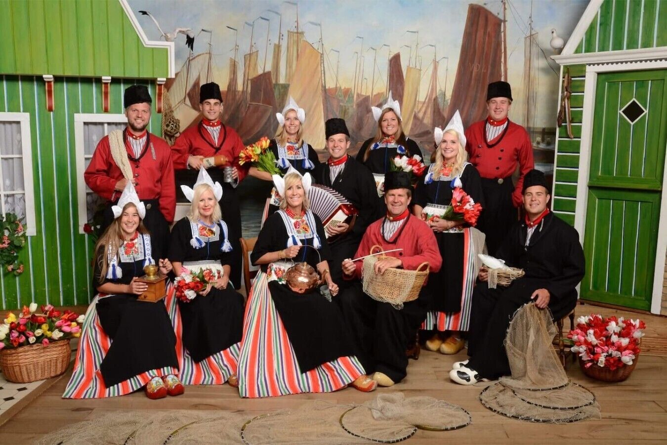 Eine Gruppe von Personen in traditioneller Kleidung posiert vor einem maritimen Hintergrund.