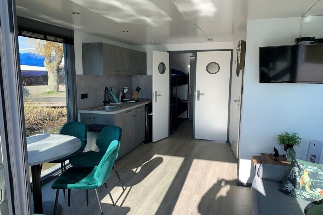 Un espacio habitable compacto con kitchenette, una zona de comedor con dos sillas, un televisor montado en la pared y una puerta que da a otra habitación.