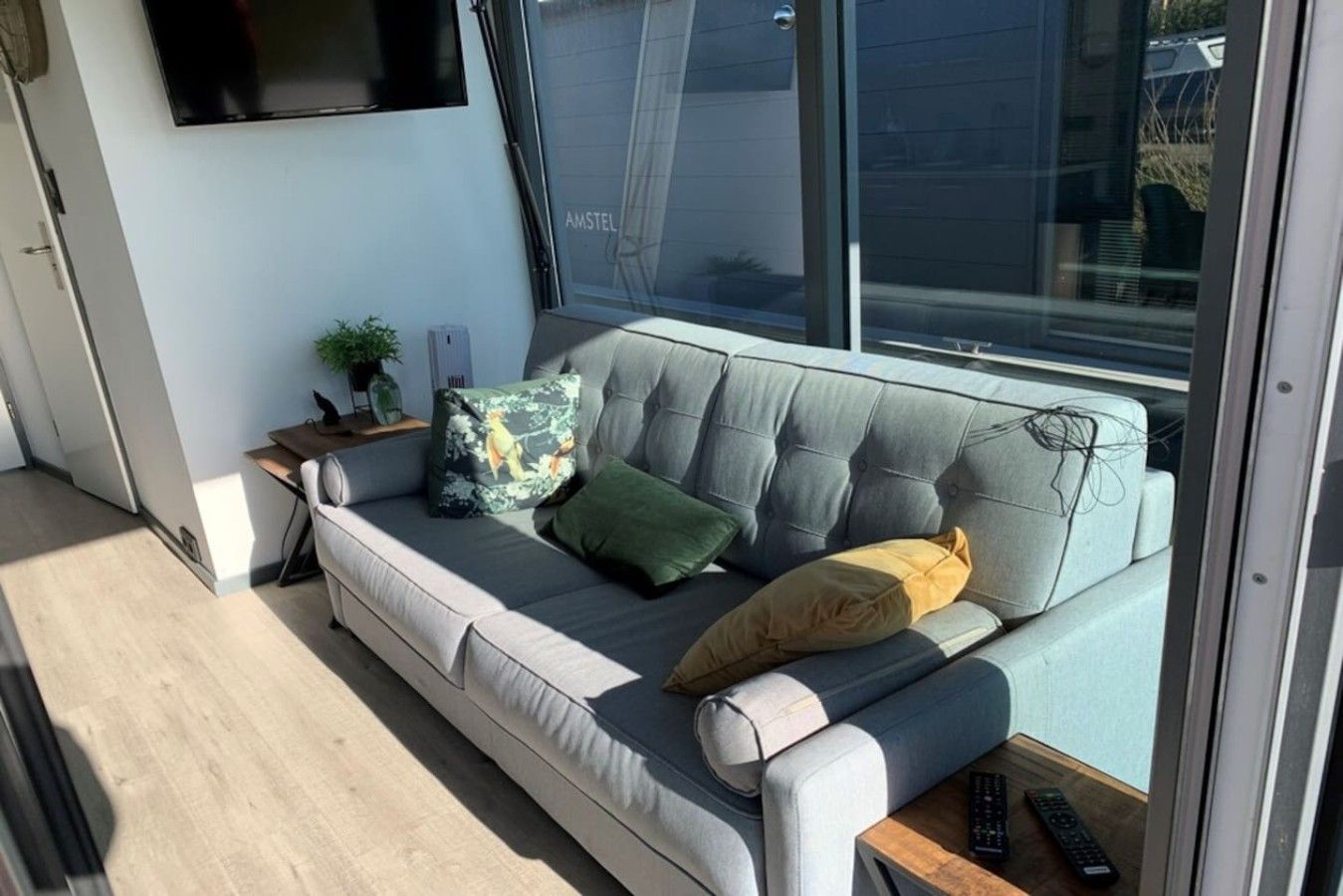 Una sala de estar moderna con un sofá gris, un televisor de pantalla plana montado en la pared y una ventana con vistas al exterior.