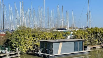 Een waterweg met een rij hoge, smalle boten, een klein huisboot afgemeerd en weelderige begroeiing op de voorgrond.