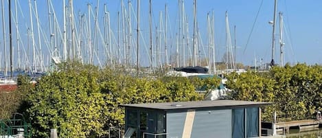 Un canal bordé d’une rangée de bateaux hauts et étroits, avec une petite péniche amarrée et un feuillage dense au premier plan.
