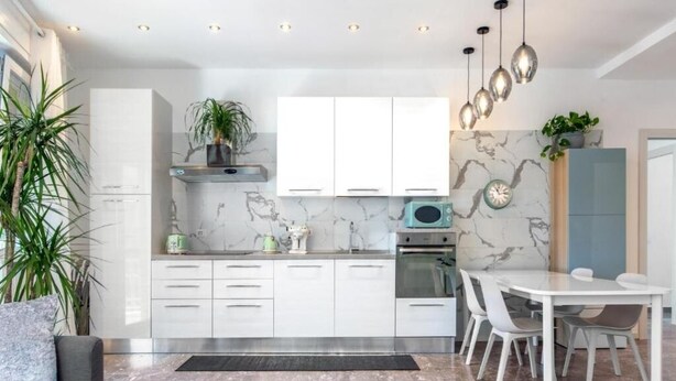 A modern kitchen with white cabinets, a marble backsplash, and a dining area with a white table and chairs.