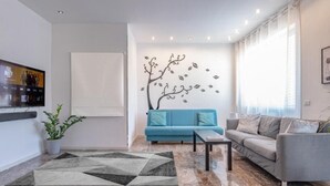 A modern living room with a blue sofa, a grey sofa, a coffee table, and a decorative wall with a tree design.