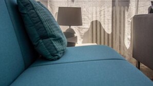 A room with a blue sofa, a teal pillow, a lamp, and a window with curtains.