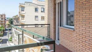 A balcony with a metal railing overlooking a street with parked cars and buildings.