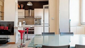 A modern kitchen with white cabinets, a built-in oven, and a coffee machine. There is a glass dining table with two chairs. - Roby's Panoramic House: A Corner of Paradise in Livorno (Livorno)