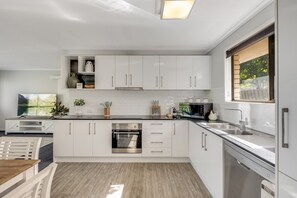 Eine moderne Küche mit weißen Schränken, Edelstahlgeräten und einem Holztisch.