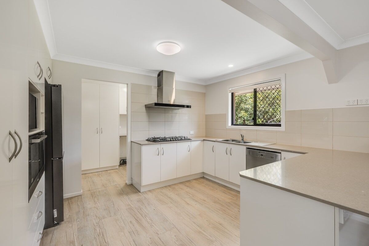A modern kitchen with white cabinetry, a built-in stove, and a window with a view of greenery.