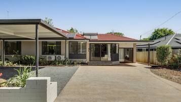 Ein modernes Haus mit überdachter Terrasse, Solaranlage und rotem Ziegeldach.