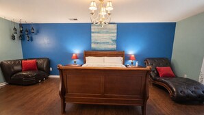 Un dormitorio con una cama de madera, dos mesitas de noche con lámparas, un candelabro, una pared azul y dos sillones de cuero.