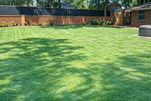 A well-maintained backyard with a brick wall, a wooden shed, and a lawn. - Clean, Quiet Private Suite w/ Hot Tub • Near Fort Benning/Midtown (Columbus)