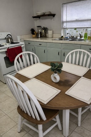 A kitchen with a round wooden table, four white chairs, a white stove, and a window with blinds. - Clean, Quiet Private Suite w/ Hot Tub • Near Fort Benning/Midtown (Columbus)
