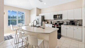 A modern kitchen with white cabinets, a central island, and a large window providing a view of the outdoors. - South Facing Pool 4 Bedroom 3 Bath Villa - Just Minutes from Disney World! (Kissimmee)