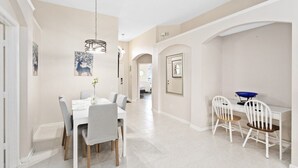 A modern dining area with a white table and chairs, a hanging light fixture, and a hallway leading to another room. - South Facing Pool 4 Bedroom 3 Bath Villa - Just Minutes from Disney World! (Kissimmee)