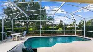 A covered outdoor swimming pool with a glass enclosure, surrounded by greenery and a lawn. - South Facing Pool 4 Bedroom 3 Bath Villa - Just Minutes from Disney World! (Kissimmee)