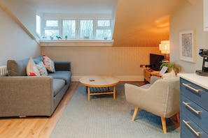 Een gezellige woonkamer met een bank, een ronde salontafel en een bureau met een lamp.