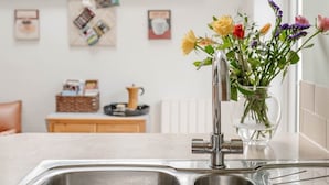 Een keuken met een dubbele spoelbak, een bloemenvaas en een koffiezetapparaat op het aanrecht.
