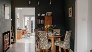 Een eethoek met een houten tafel en gestreept beklede stoelen, een boekenplank en een vaas met bloemen.