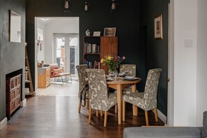 Un coin repas avec une table en bois et des chaises à motifs, une bibliothèque et un vase rempli de fleurs.